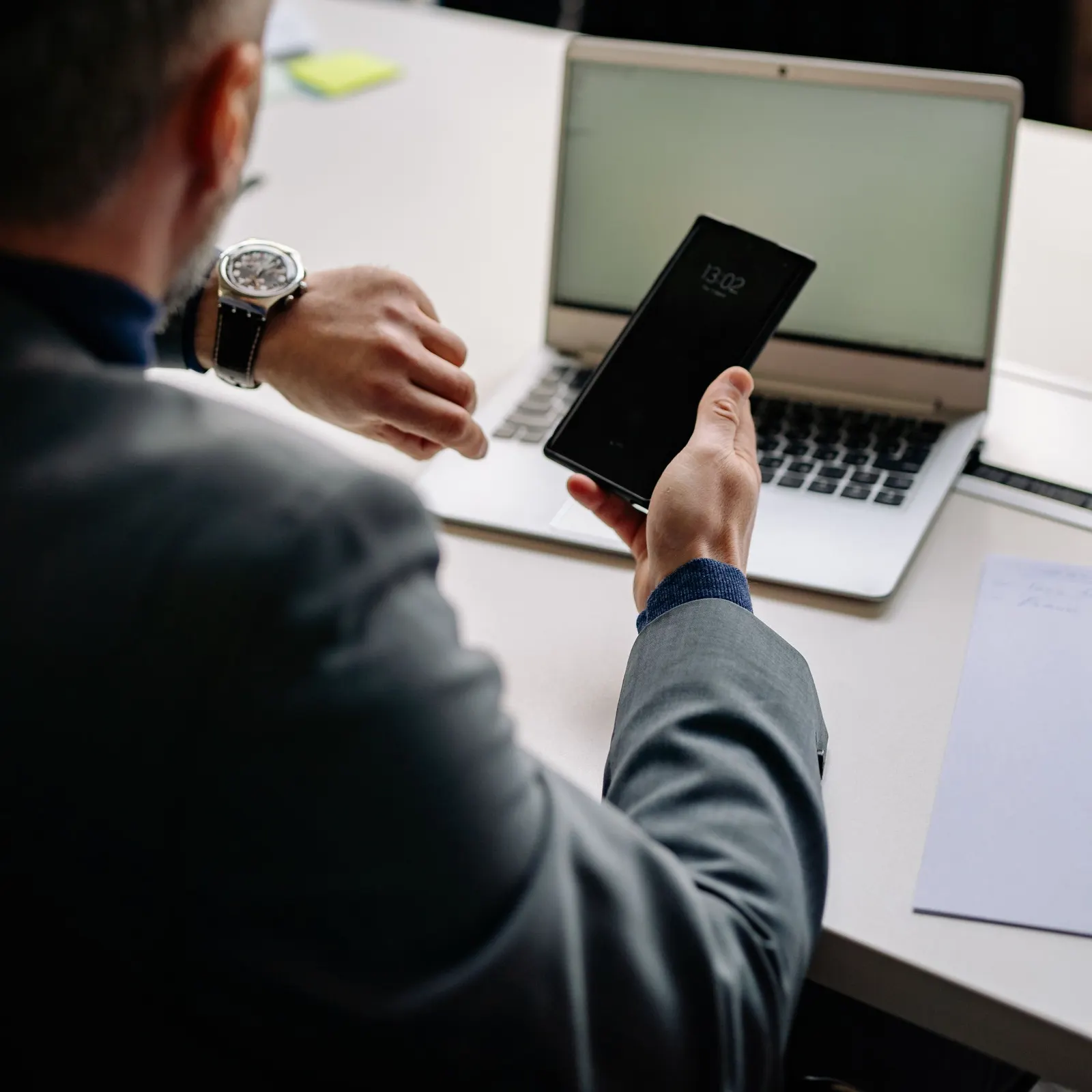 A professional glancing at a phone notification between laptop meetings at a desk.
