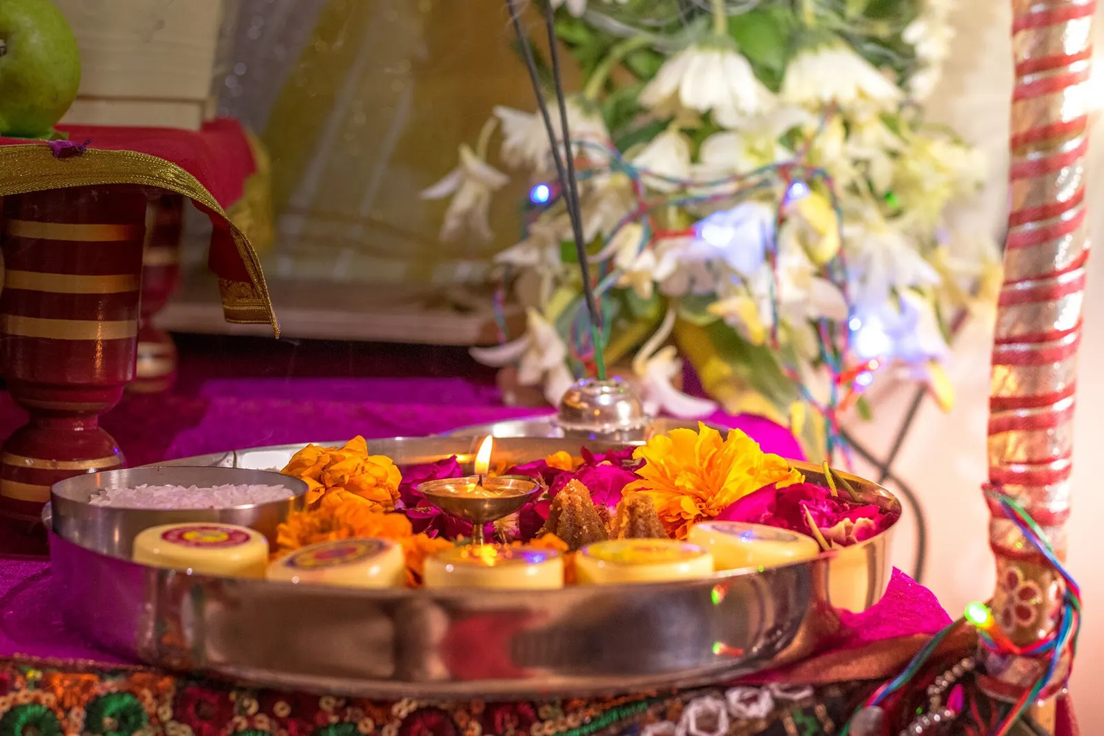 A puja thali with a lit diya arranged in a home living room.