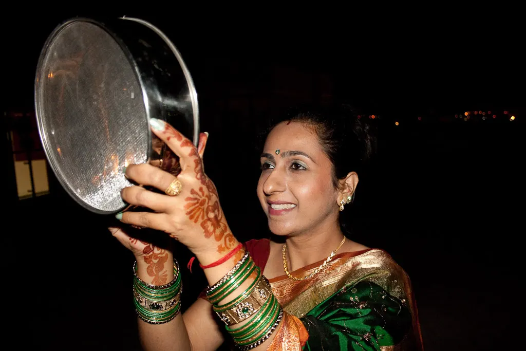A woman performing the traditional sieve ritual to view the moon on Karva Chauth night.