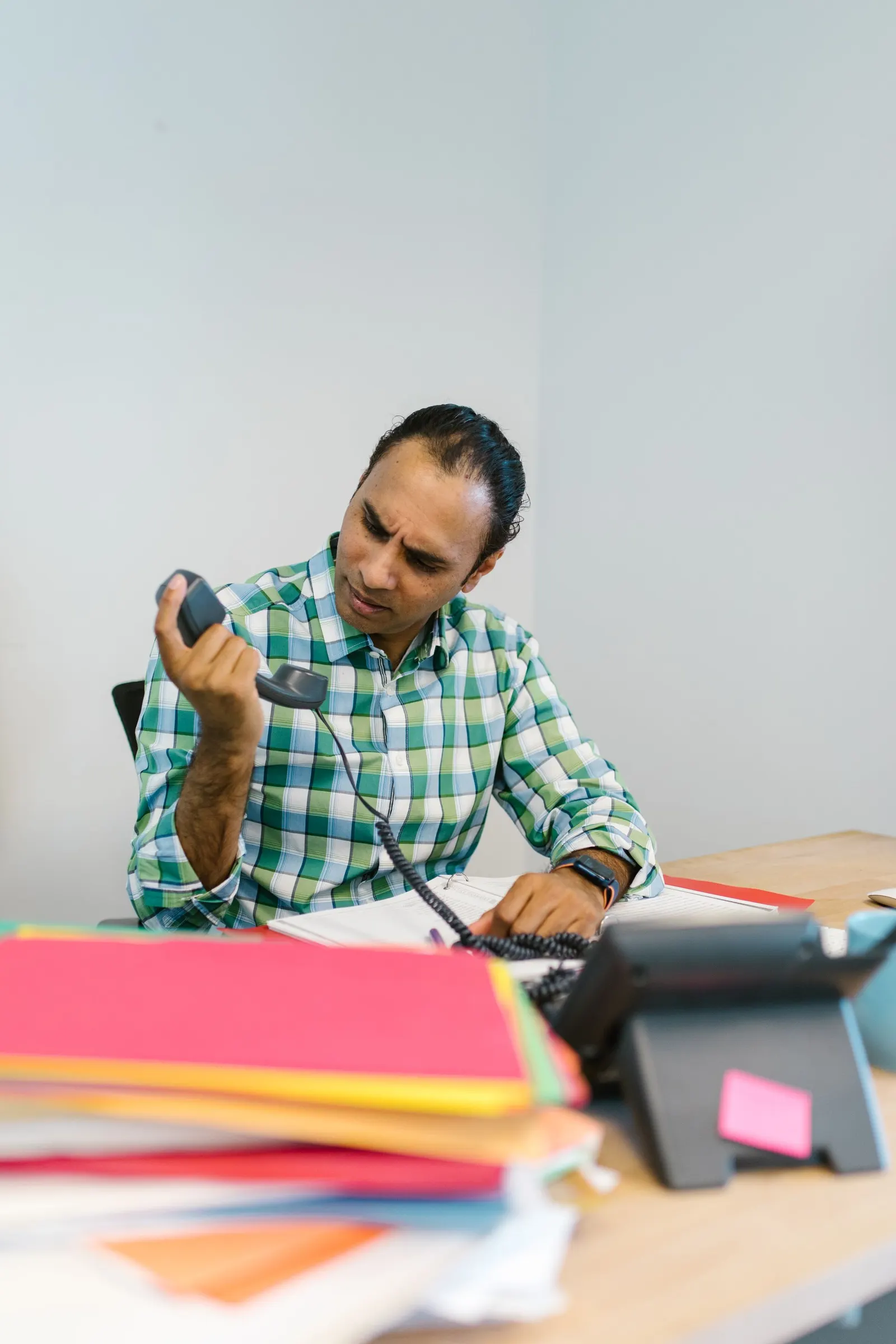 A person checking documents and a phone at a desk, appearing anxious.