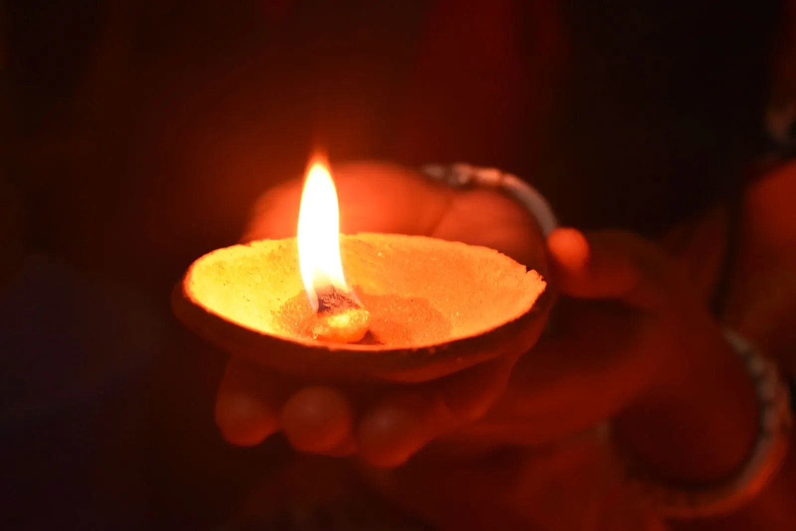 Hands lighting a small oil lamp at dusk.