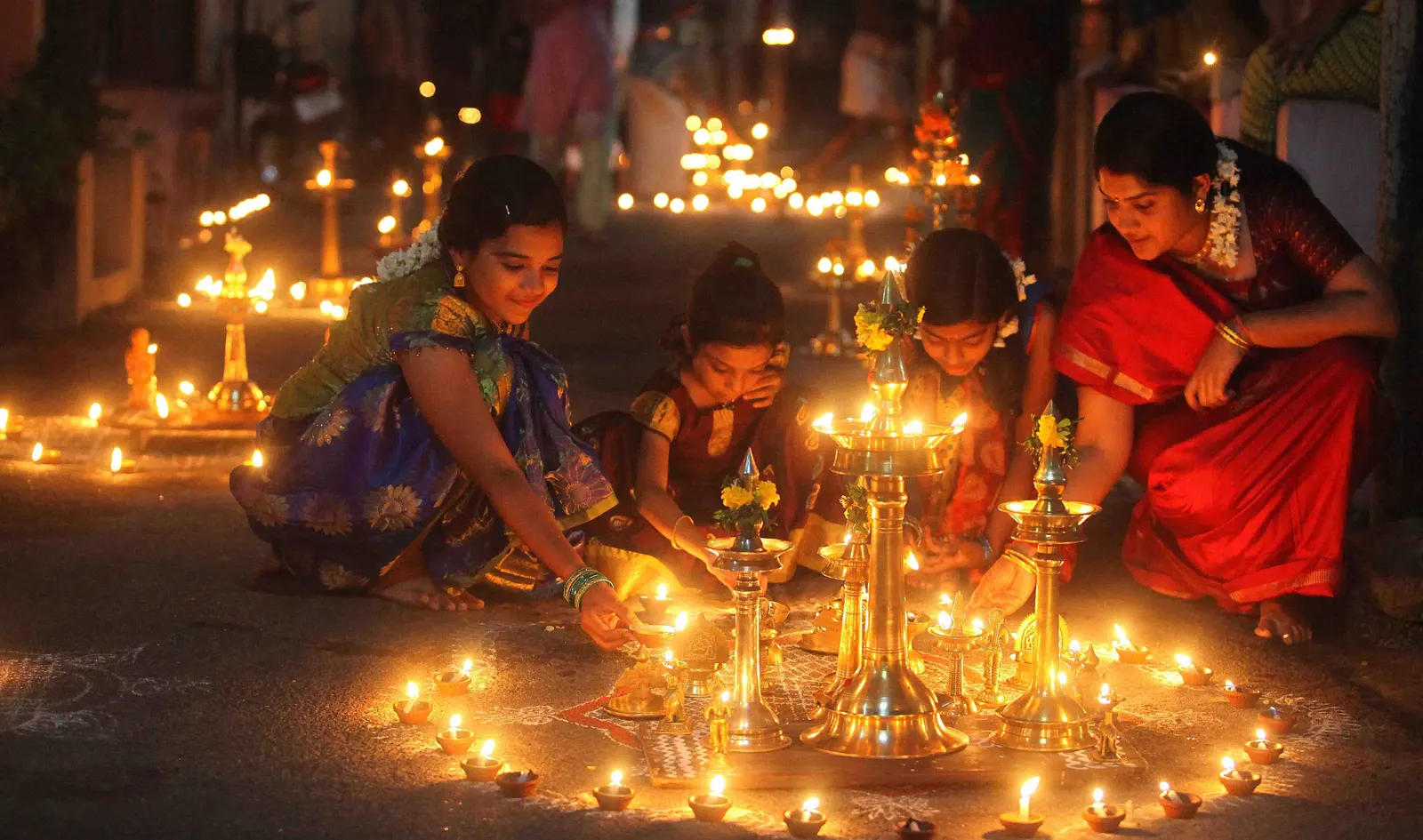 A young child lighting a diya lamp during a home puja in the United States.