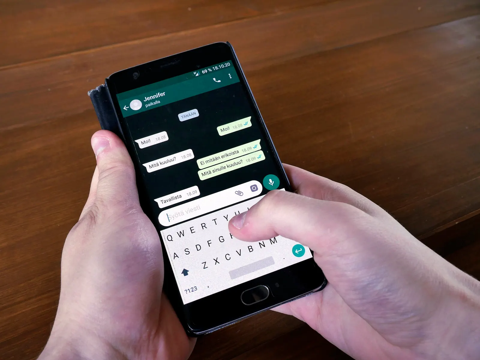 A hand holding a phone with a WhatsApp chat open at night.