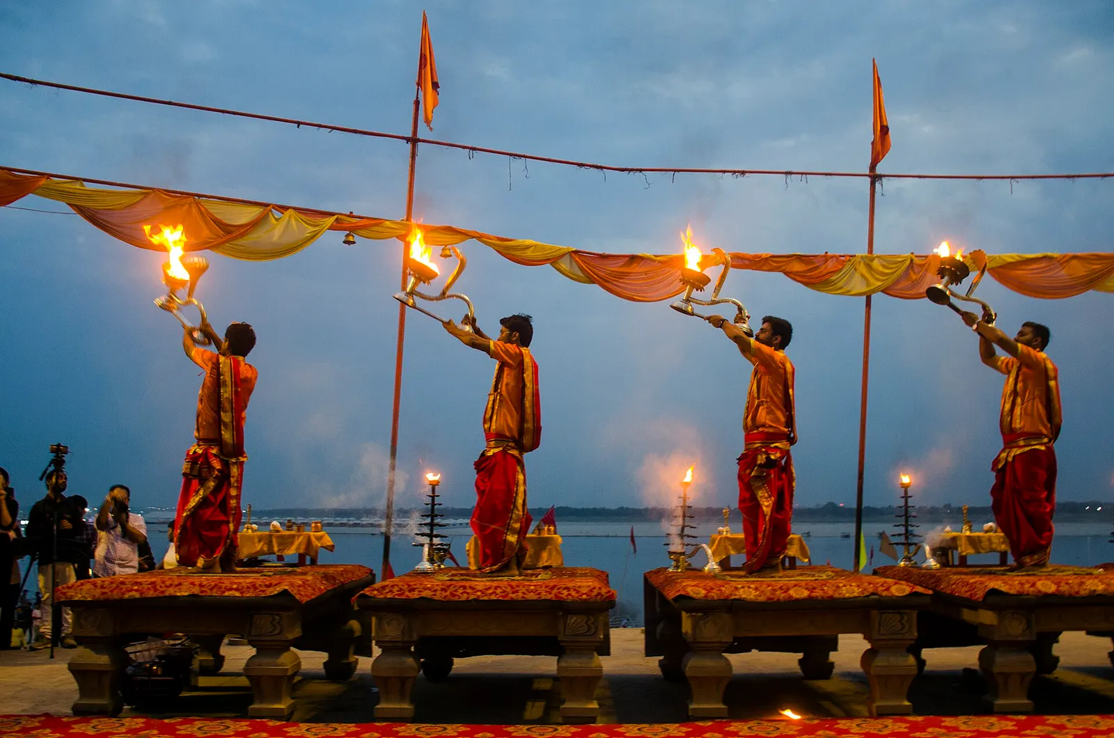 A pandit performing aarti rituals at a river ghat at sunrise.